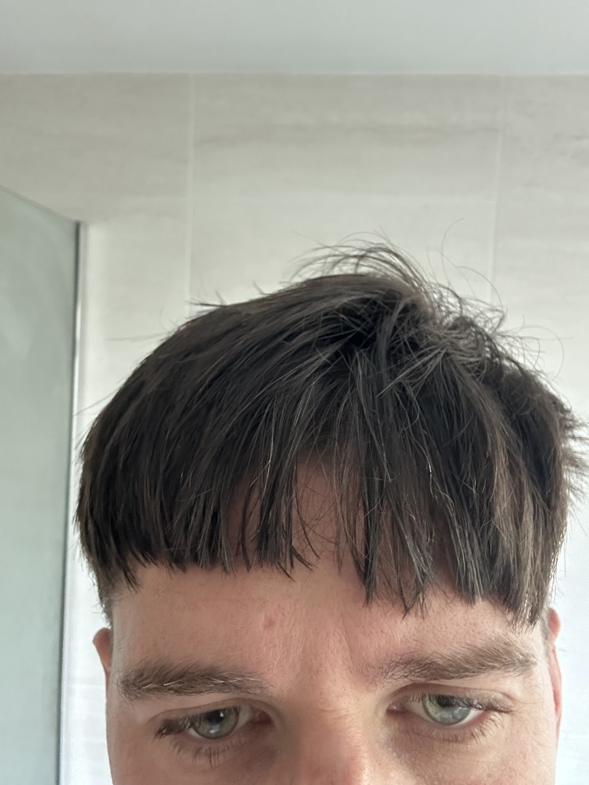 Close-up of a freshly cut textured fringe against a white tiled wall